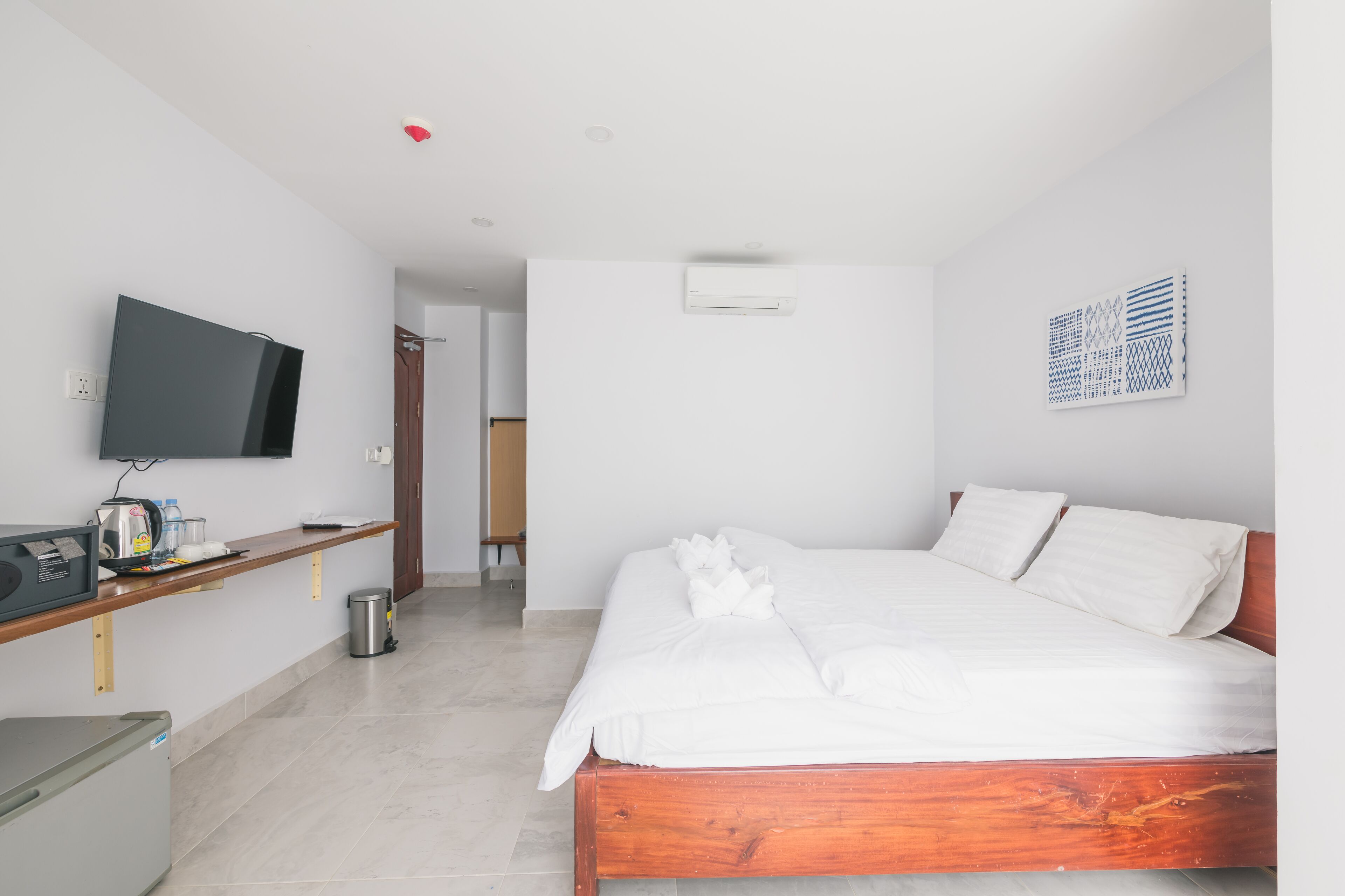 Et moderne hotelværelse med en træseng, et fladskærms-tv, et skrivebord med en computer og en skraldespand.