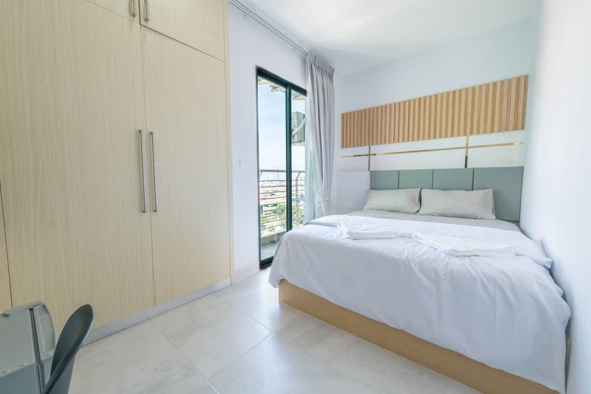 A modern bedroom with a large bed, a wardrobe, and a sliding glass door leading to an outdoor balcony.