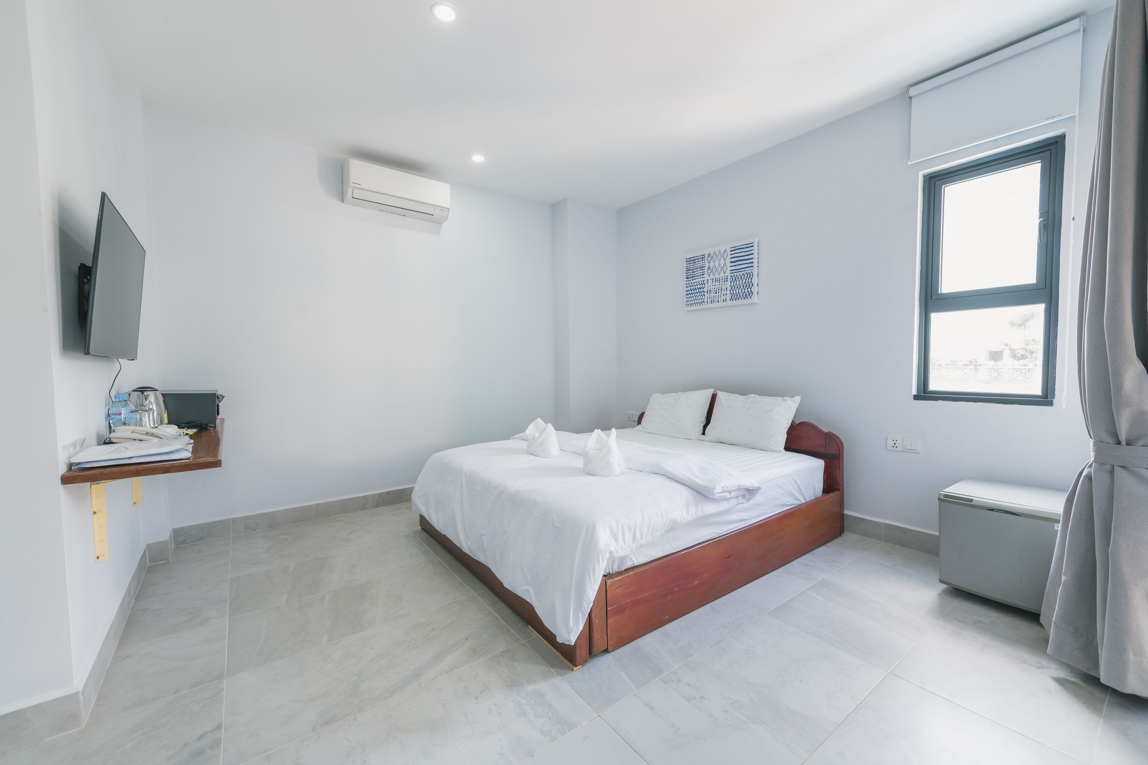 Quarto moderno com cama, televisão, prateleira pequena e janela.