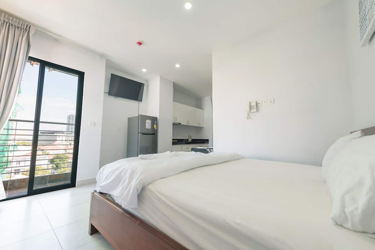 A modern hotel room with a large bed, a kitchenette, a flat-screen TV, and a sliding glass door to the balcony.