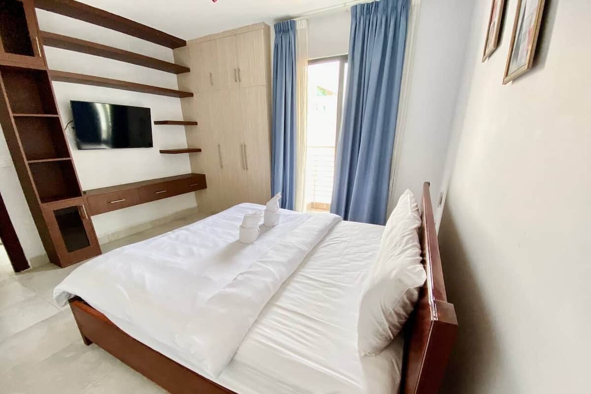 A neatly made bed with white linens and pillows, a wooden headboard, and a built-in TV shelf.