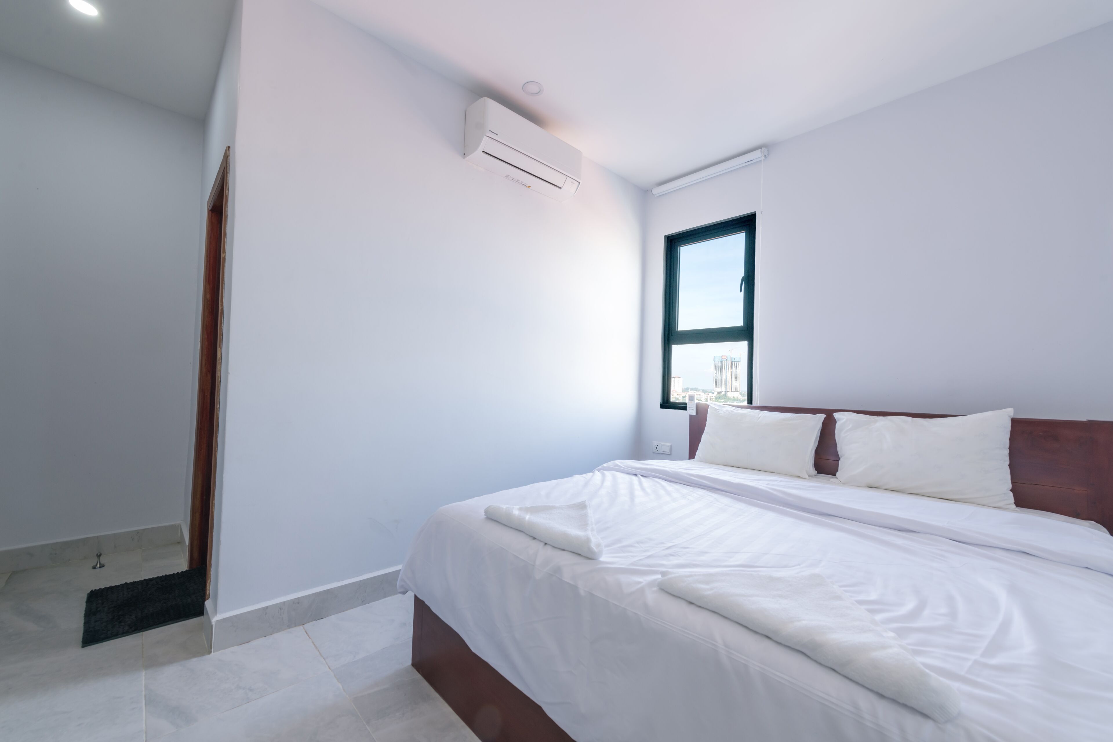 A modern bedroom with a large bed, a window, and an air conditioning unit.