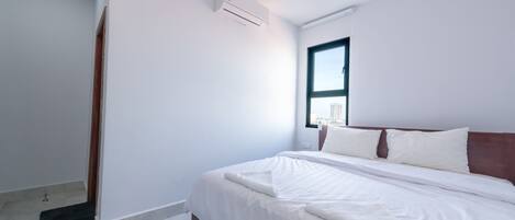 A modern bedroom with a large bed, a window, and an air conditioning unit.