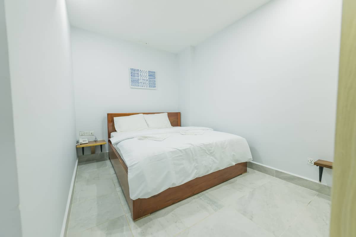 A bedroom with a wooden bed, white bedding, a small bedside table, and a wall-mounted artwork.