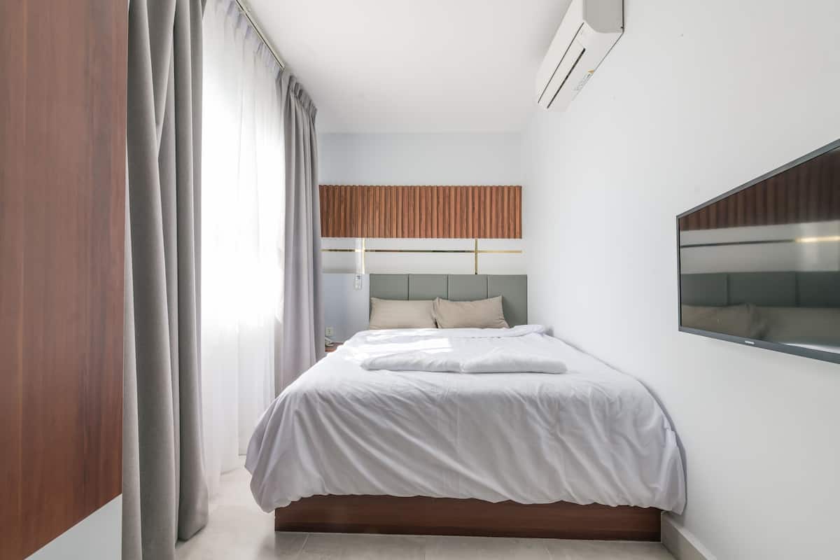 A modern bedroom with a bed, curtains, a headboard, and a wall-mounted air conditioner.