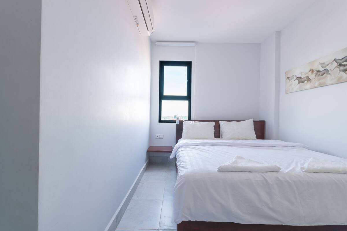 A modern bedroom with a large bed, a window, and a painting on the wall.