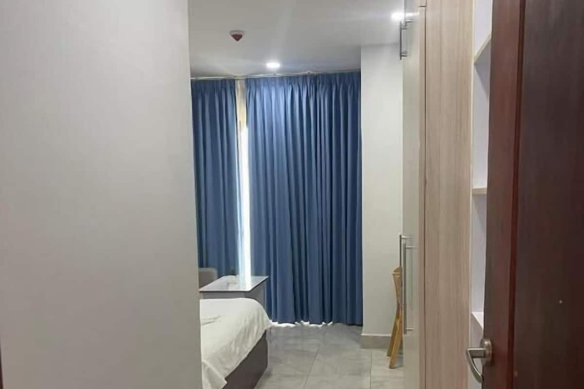 A narrow hallway leading to a bedroom with a bed, a blue curtain, and a wooden door.
