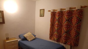 Une petite chambre simple, avec un lit simple, une table de chevet et un rideau à motifs.
