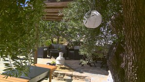 Un espace extérieur aménagé en terrasse, avec une table en bois, un chemin de pierres et un coin salon comprenant un canapé et une table basse.