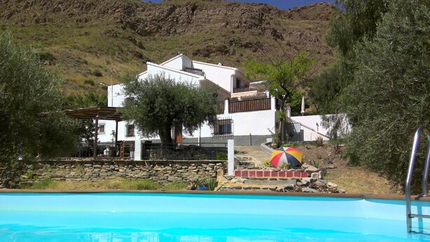 Une piscine avec vue sur un bâtiment blanc et une colline en arrière-plan.