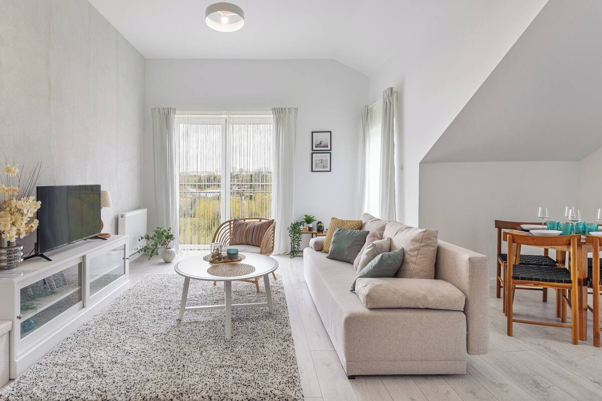 A modern living room with a sofa, coffee table, and a dining area with a table and chairs.
