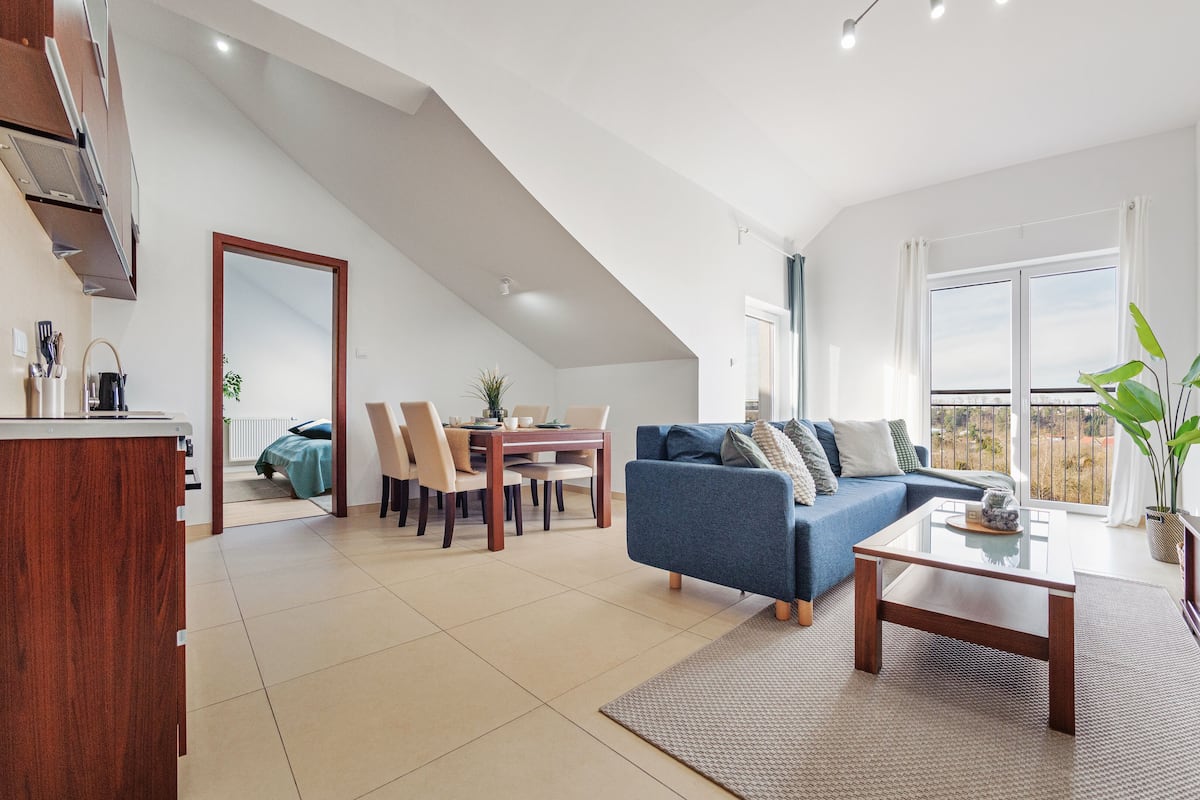 A spacious living area with a dining table, blue sofa, and a large window offering a view.