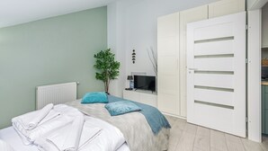 Een slaapkamer met een bed, een radiator, een televisie, een plant en een kledingkast.