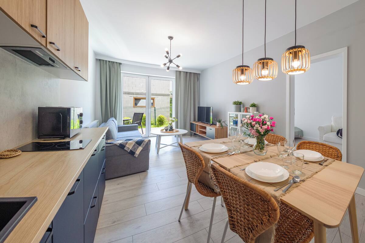A modern kitchen with a built-in oven, a dining area with a table set for four, and a TV in the background.