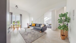 Een moderne woonkamer met een grijze bank, een eettafel met stoelen en een groot raam met gordijnen.