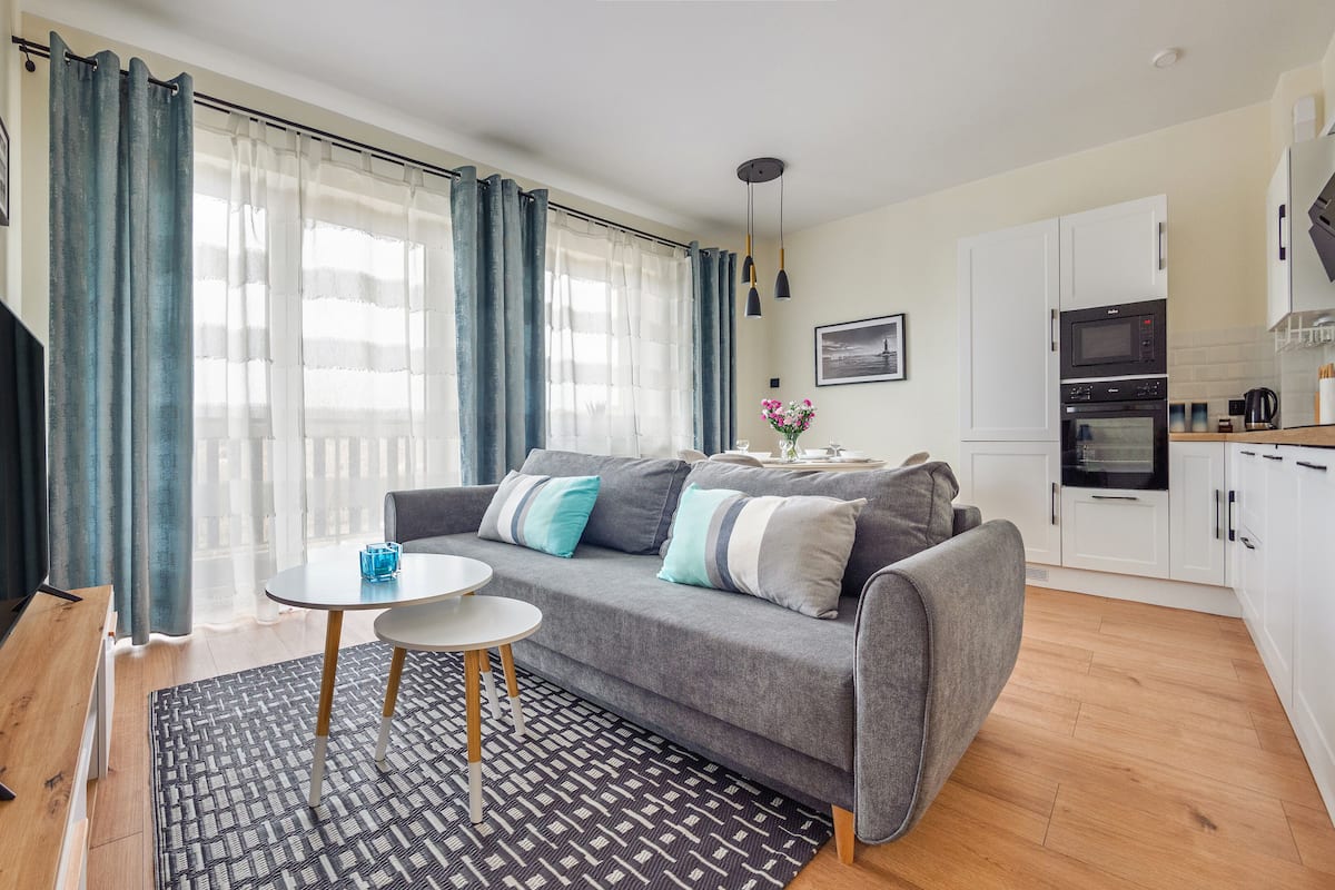 A modern living room with a grey sofa, a small round table, and a TV on a stand.