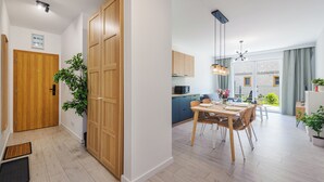 Een modern appartement met een houten deur, een eethoek met tafel en stoelen, en een keuken met een magnetron.