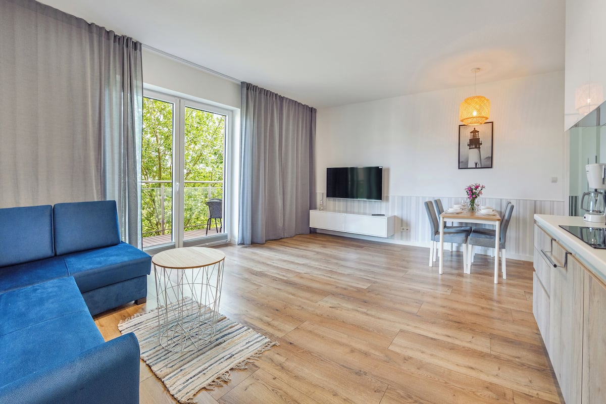 A modern living room with a blue sofa, a small round table, and a TV on a white cabinet.