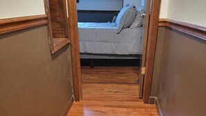 Un estrecho pasillo con suelo de madera que conduce a un dormitorio con una cama y un cuadro en la pared.