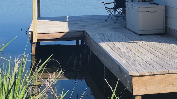 Un muelle de madera que se adentra en aguas tranquilas, con una zona de estar cubierta y un enfriador al lado derecho.