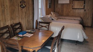 Una habitación con pared de madera, una cama con edredón blanco, una mesa de comedor de madera con sillas y una lámpara en el techo.