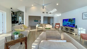 Uma sala de estar espaçosa, com uma televisão de tela plana grande, assentos confortáveis e um ventilador de teto moderno.