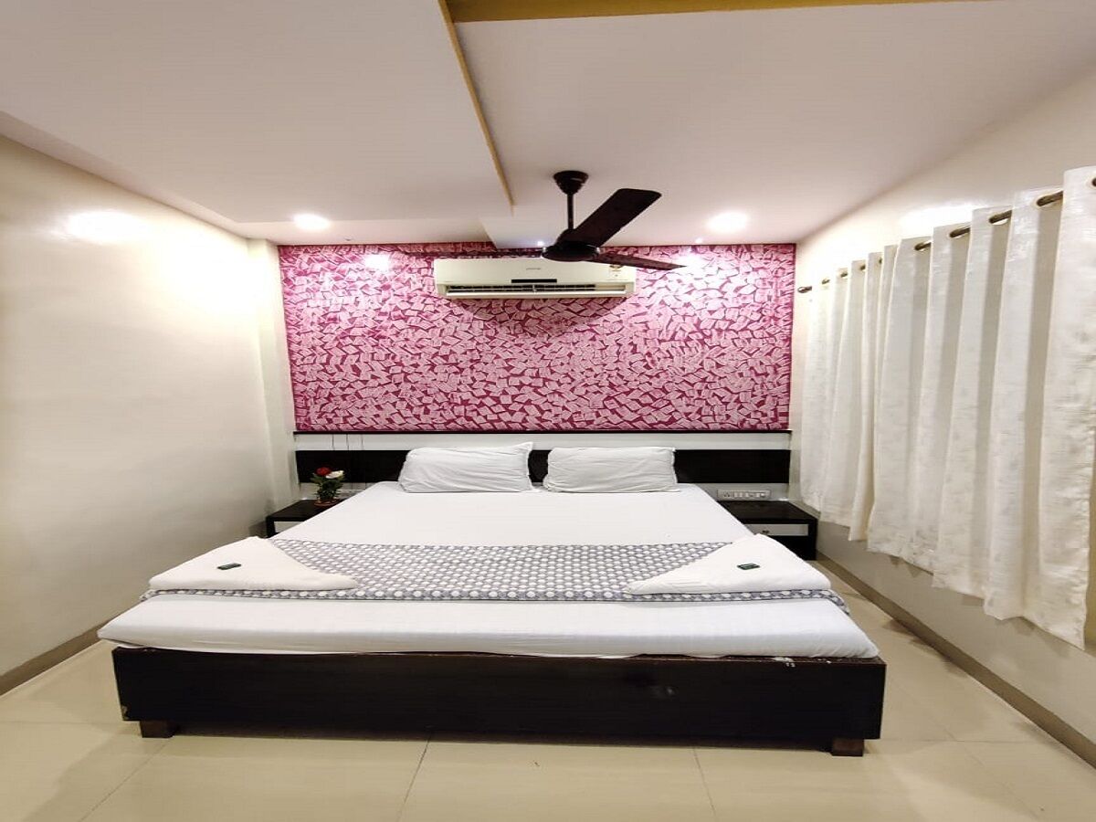 Un dormitorio con cama, ventilador de techo, aire acondicionado, mesita de noche y ventana con cortinas.
