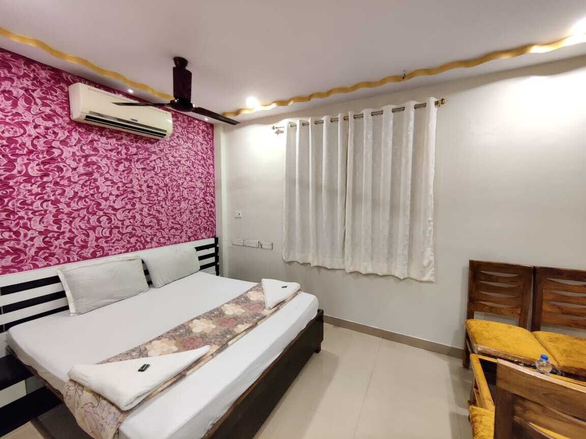 Quarto com cama, mesa de cabeceira, guarda-roupa, ar condicionado e janela com cortinas.