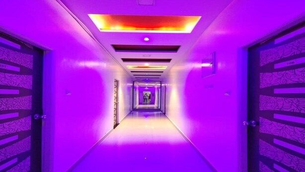 Un pasillo con tonalidades moradas, que presenta una lámpara central y puertas con diseños.