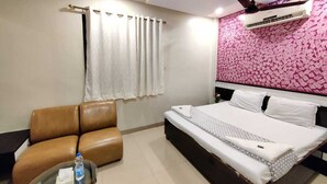 Una habitación de hotel con una cama, un sofá de cuero marrón, una mesa de centro de cristal con una botella, cortinas y una pared con estampado.