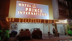 Hotel Prince International con un gran letrero iluminado, dos coches estacionados frente a él y una persona de pie cerca de la entrada.