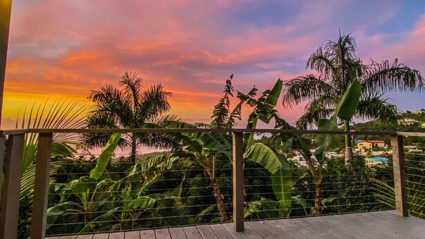 Un balcon offrant une vue sur le coucher de soleil, entouré d’une végétation tropicale luxuriante.