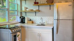 Une cuisine avec des meubles blancs, un réfrigérateur en acier inoxydable, une cuisinière et des étagères ornées de plantes et de vaisselle.