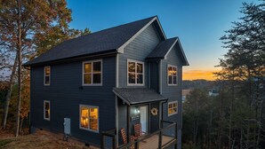 A two-story house with a porch, a welcome sign, and a view of the surrounding forest.