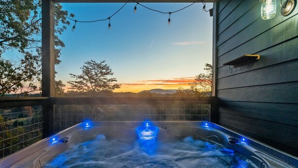 A hot tub with blue lighting, surrounded by a wooden deck and a view of a sunset.