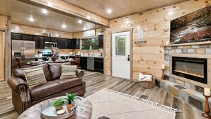 A cozy living room with a brown leather couch, a round coffee table, and a fireplace.