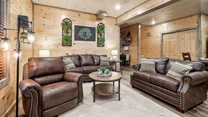 A cozy living room with a brown leather sectional sofa, a round wooden coffee table, and a wooden ceiling.