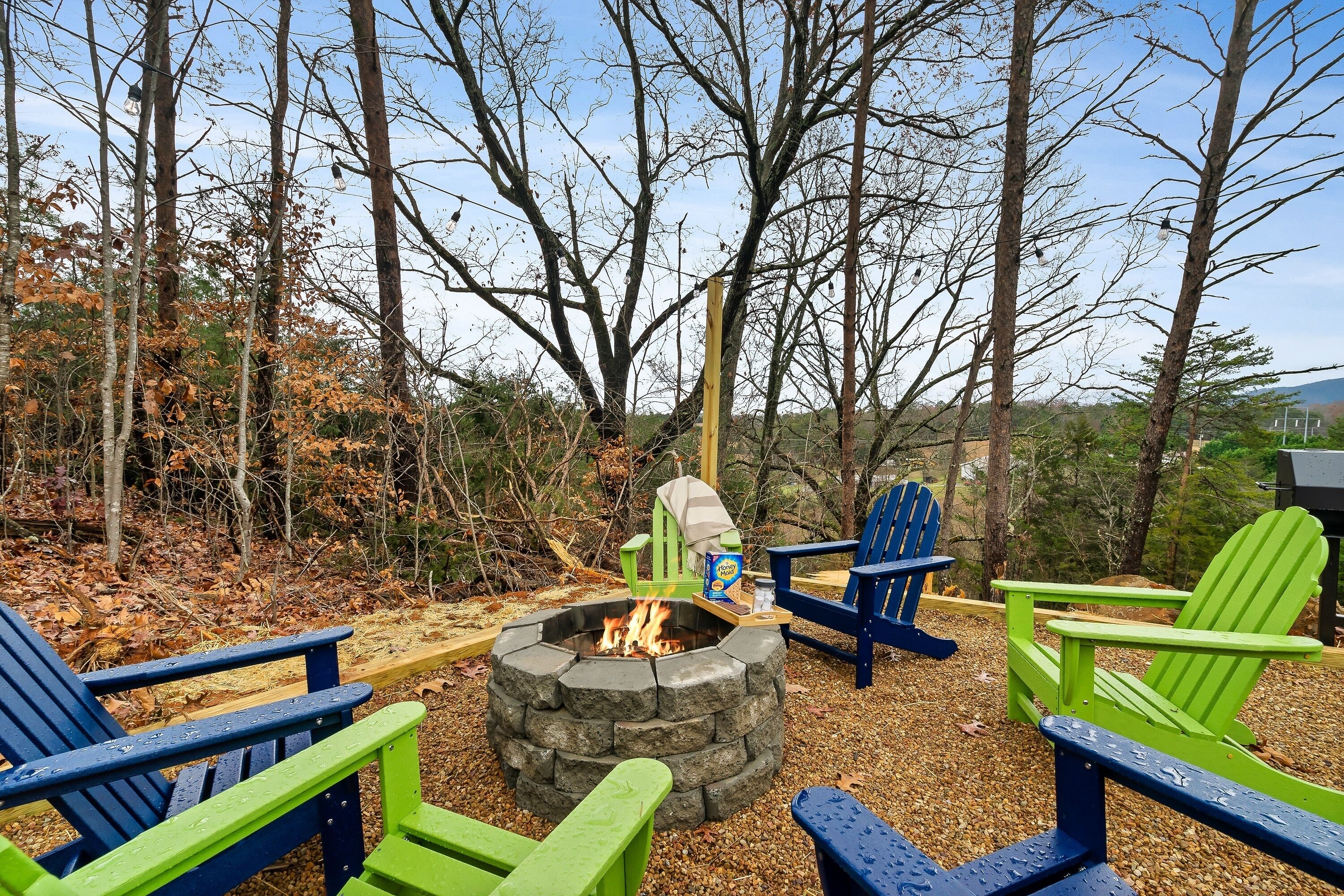 A fire pit surrounded by Adirondack chairs in a wooded area.