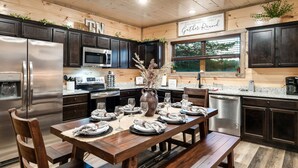A modern kitchen with dark cabinets, stainless steel appliances, and a wooden dining table set for six.