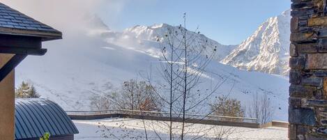A snow-covered mountain landscape with a stone building and a metal roof structure in the foreground.