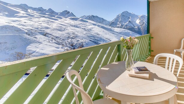 Un balcón con vistas a montañas nevadas, una mesa redonda con sillas y un jarrón con flores.
