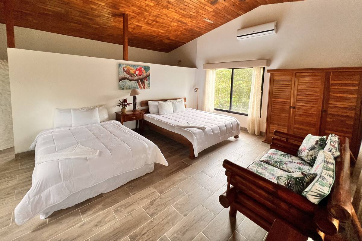 A bedroom with two beds, a wooden ceiling, a ceiling fan, a window with curtains, and a wooden wardrobe.