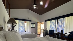 A spacious bedroom with a large bed, a desk, and a chair. There is a window with curtains and a view of the outside. - Blue Banyan Inn (Naranjito)