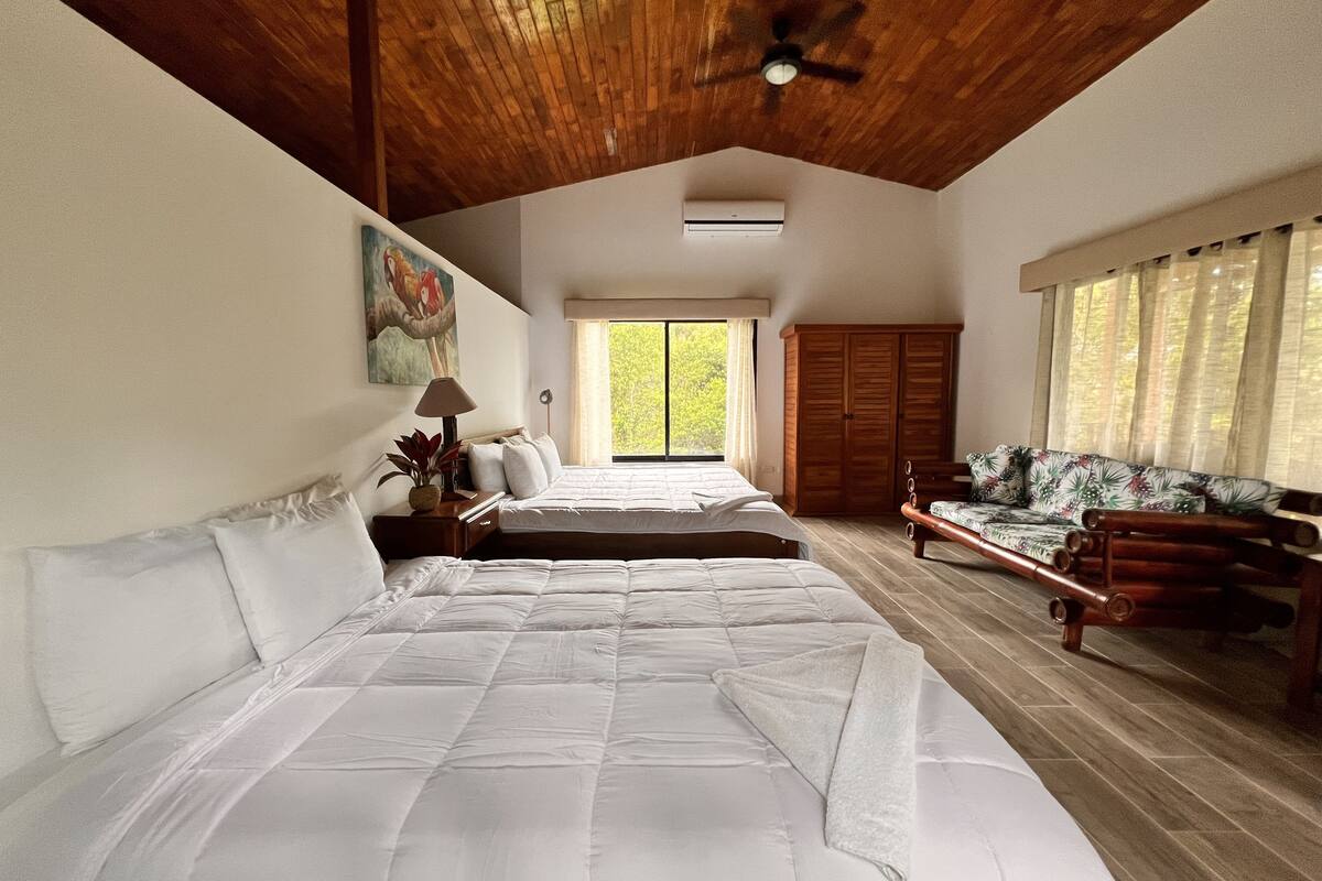 A bedroom with two beds, a wooden ceiling, a large window, and a wardrobe.