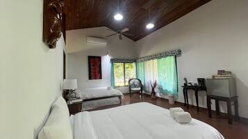 A hotel room with two beds, a ceiling fan, a desk with a chair, and a window with curtains.