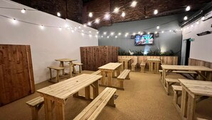 A cozy indoor seating area with wooden tables and benches, string lights, and a TV screen on the wall. - The Hoptimist  (Stockton-on-Tees)