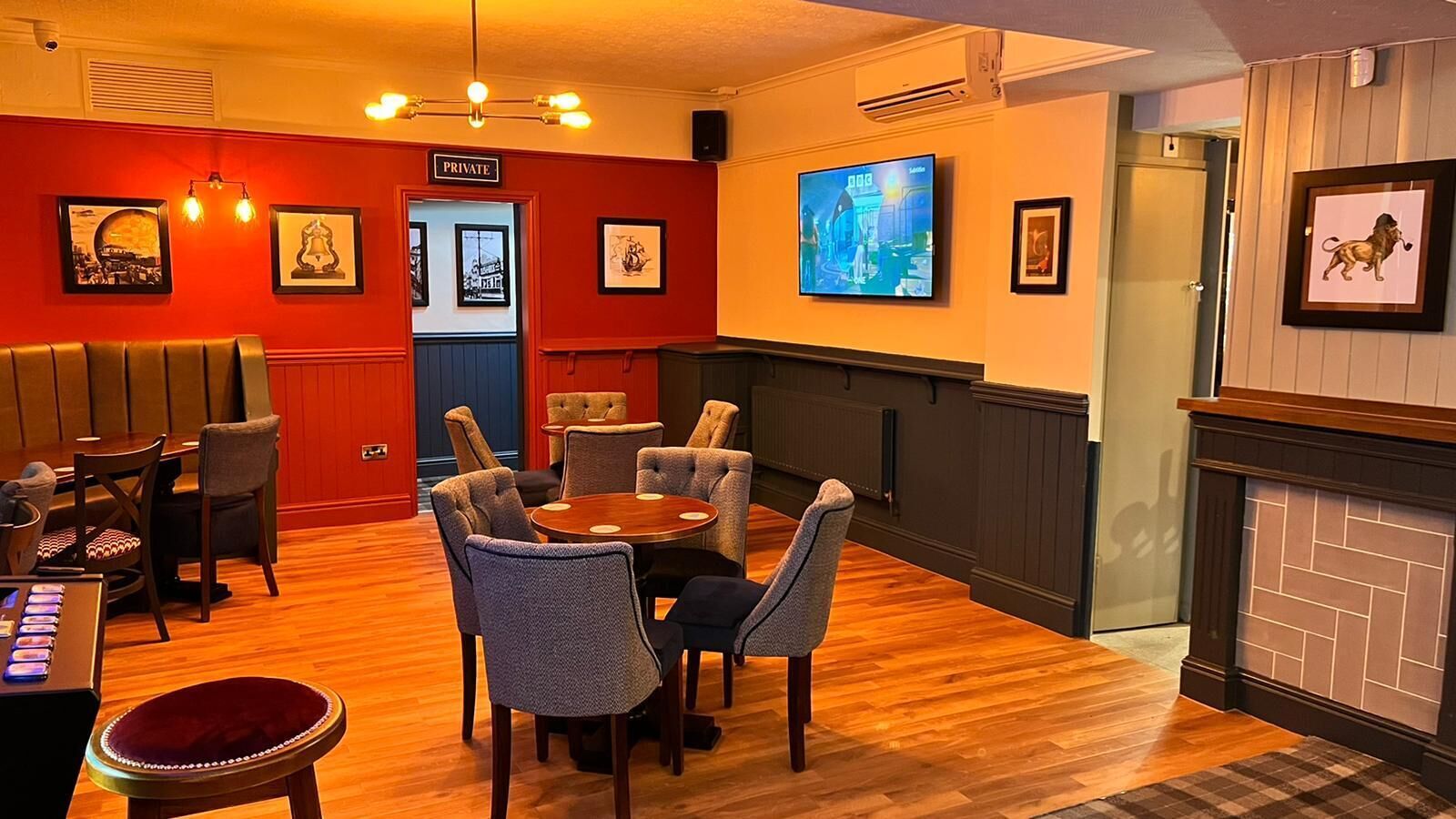 A cozy room with a wooden floor, a round table with chairs, a fireplace, and framed pictures on the walls.