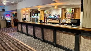 A bar area with a checkered floor, a counter with a cash register, and a wall of liquor bottles. - The Hoptimist  (Stockton-on-Tees)