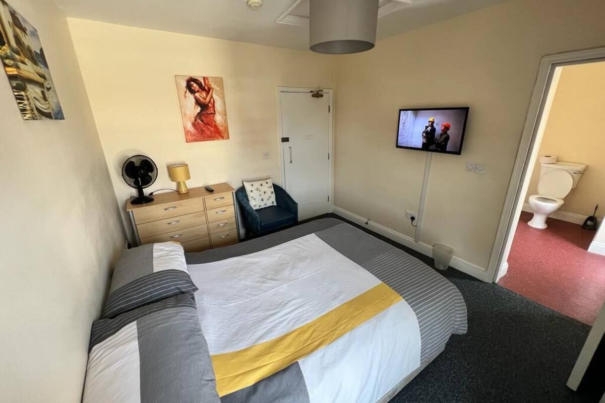 A bedroom with a bed, a dresser, a television, and a door.