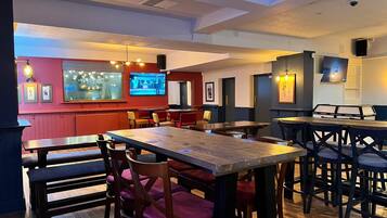 A restaurant with wooden tables and chairs, a television screen, and framed pictures on the walls.
